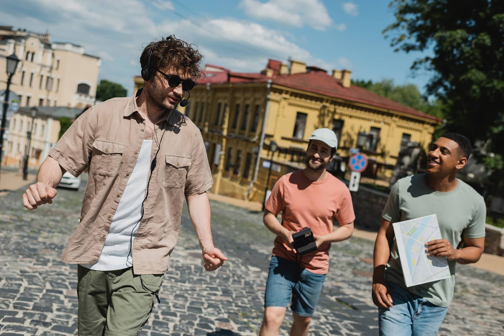 young tour guide in sunglasses and headset walking with cheerful multicultural tourists on Andrews