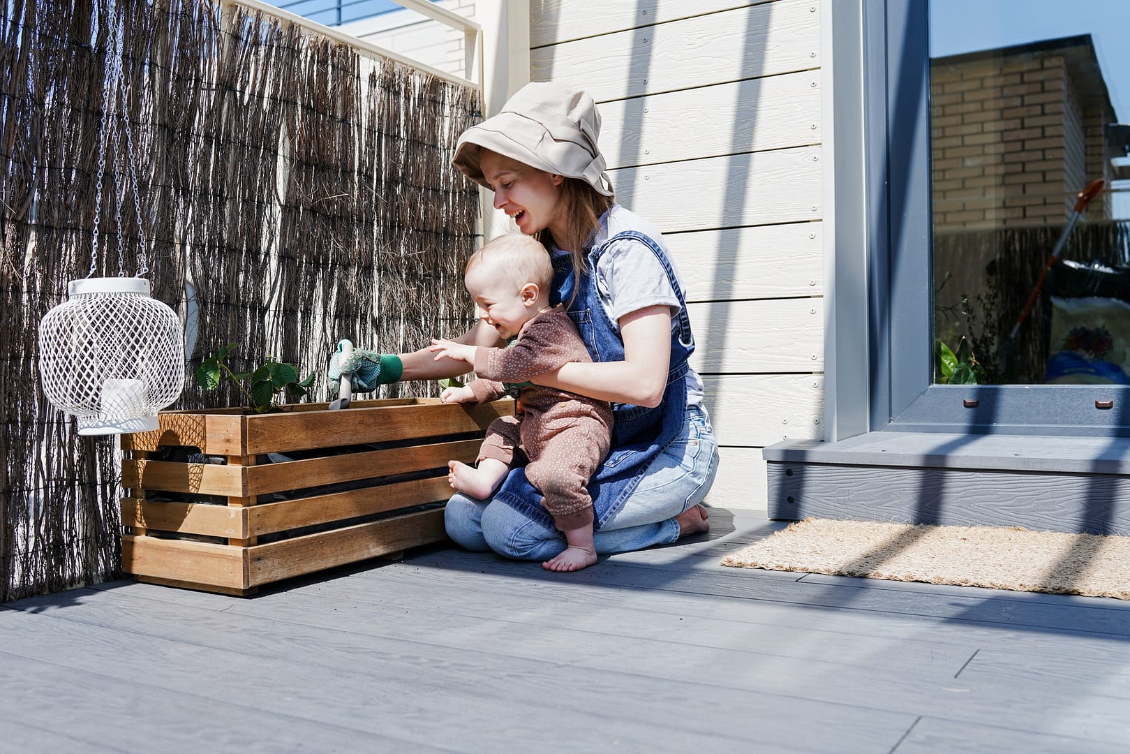 Mother and her little baby transplanting young strawberry on rooftop terrace at sunny spring day