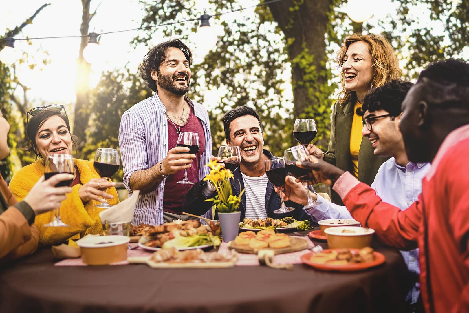 Group of friends dining outdoors toasting with red wine in the backyard