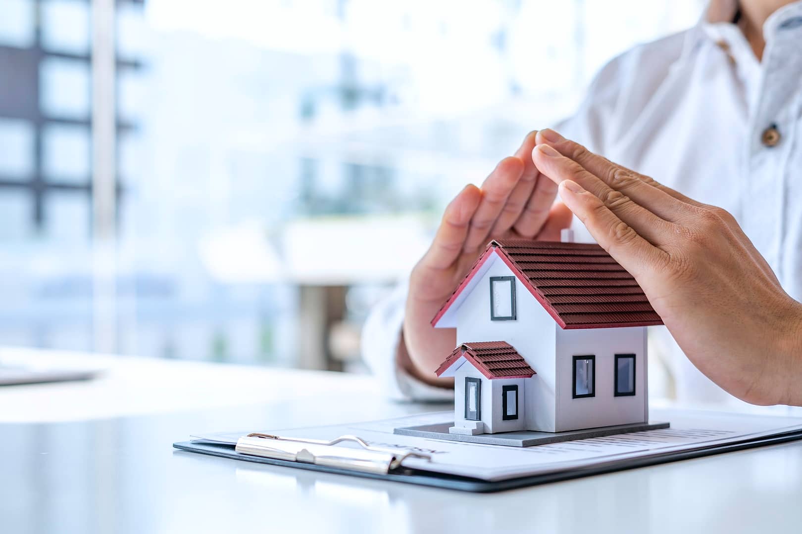 Home security and insurance concept - A close-up view of a man defending a home model by hand on a t