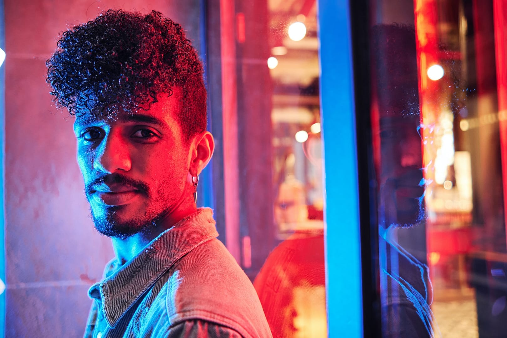 young hispanic man close to a neon light with blue and red lights