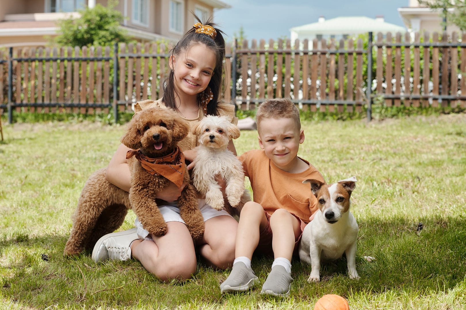 Two cheerful siblings playing with their cute dog pets on backyard